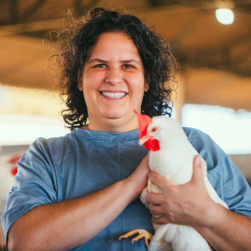 Mulher sorrindo enquanto segura uma galinha branca em suas mãos