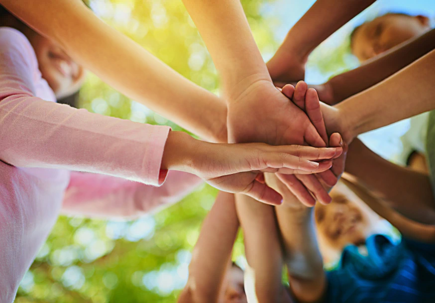 Várias mãos sobrepostas em gesto de união e trabalho em equipe sob luz natural